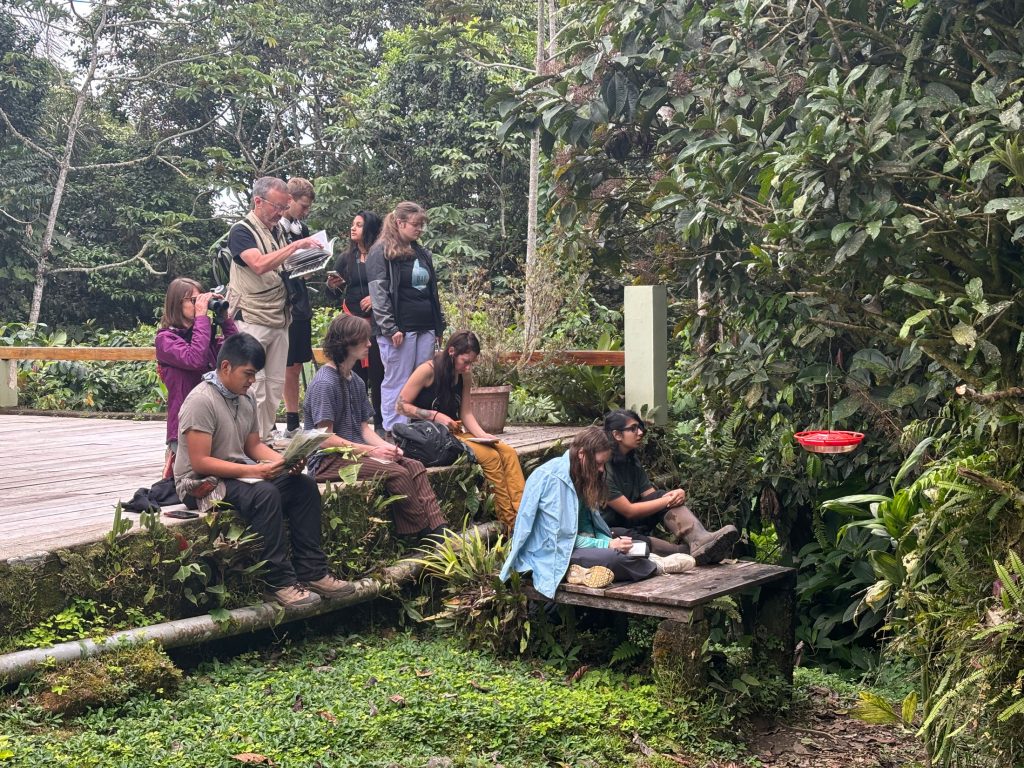 On the deck of Wildsumaco Lodge, students learn about hummingbirds from instructor Travis Knowles of Francis Marion University. Their final exam tested their understanding of ecological concepts rather than identification of species. Justin V. Bartolon is seated closest to the camera on the deck at left, and Aislinn-Anne Brown is seated on the small platform and wrapped in a blue shirt. Photo by Leslie Costa, provided by Smokies Life.