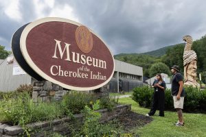 Museum Director of Education Dakota Brown (Eastern Band of Cherokee Indians) and artist Luke Swimmer (Eastern Band of Cherokee Indians) consider the museum’s previous sign. The museum recruited Swimmer to use his unique artistic style to update the sign by painting over the old name and visuals with a contemporary design to signal the museum’s new name and direction. Image courtesy Museum of the Cherokee People.