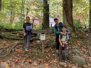 E. C., Jennifer, and Landon Stewart take a break by a sign marking 7.6 miles left on their final Smokies 900 Miler hike. Photo by Korrin Bishop.