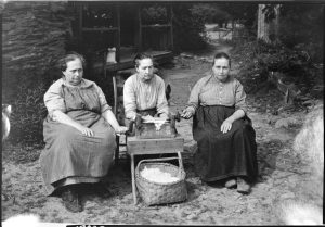Three of the Walker sisters (from left, Hettie, Martha, and Louisa) use a cotton gin outside their cabin, which still stands today. Photo courtesy of Great Smoky Mountains National Park archives.