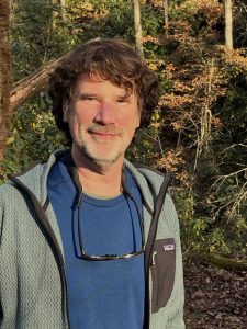 Close up photo of Steve Kemp in a blue tshirt and gray fleece jacket with sunglasses around his neck.