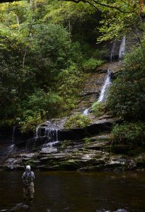 A fisherman at the base of a waterfall