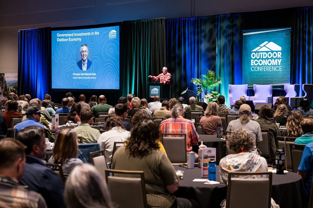 Photo of a man standing at a lectern in front of a crowd of people.