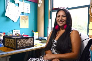 A smiling woman sitting at a desk in front of a window