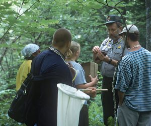 Man in ranger outfit shows an insect to a group of people including one who is holding an insect net