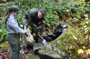 A male and female forest ranger picking up trash and shoveling a fire ring.
