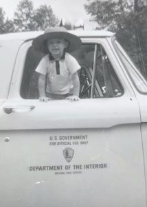 A young boy in a ranger hat leans out the winder of an NPS truck.