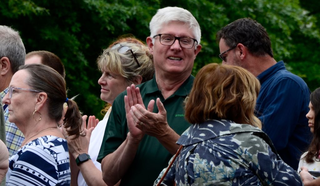 A man wearing a green pop shirt and glasses claps his hands
