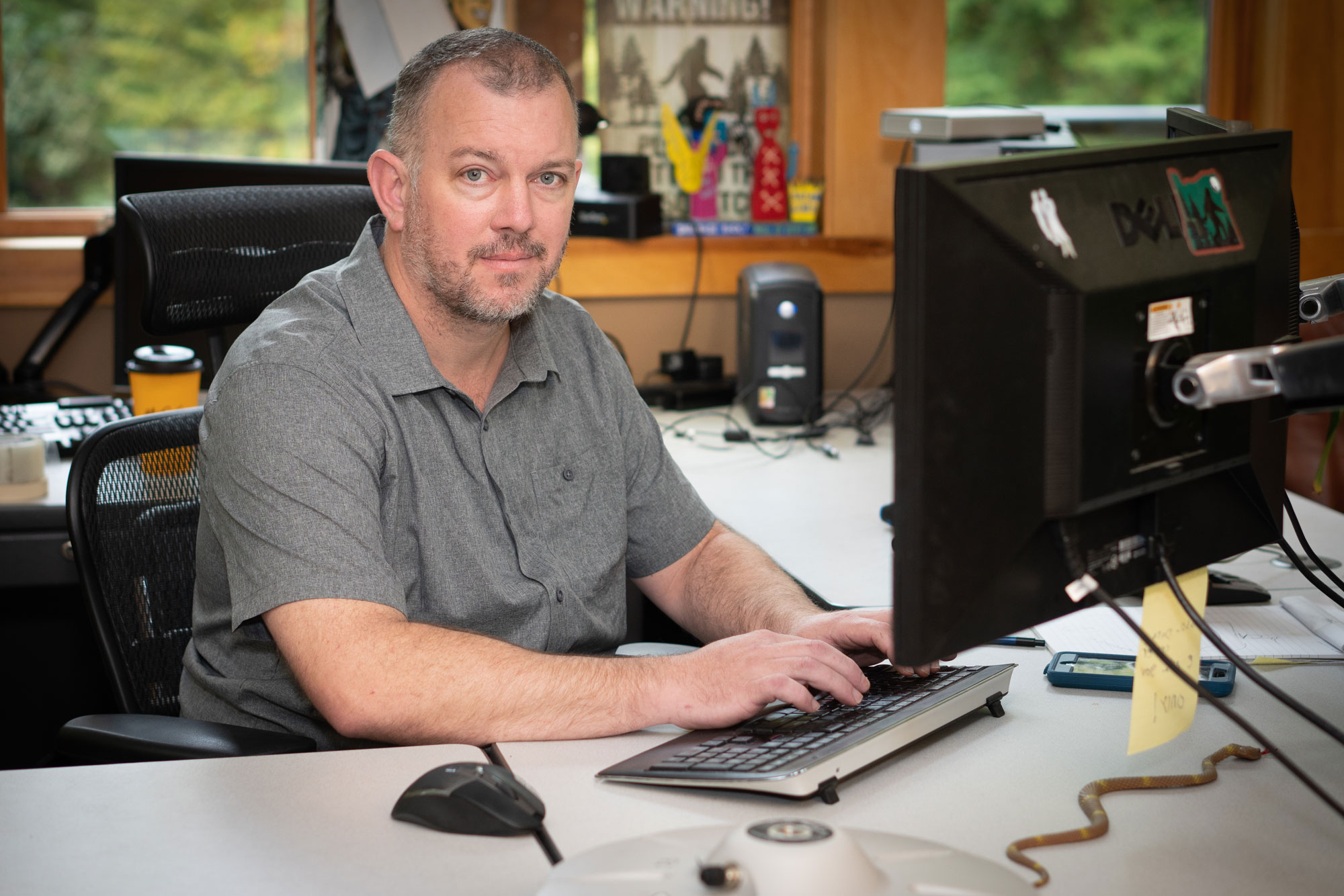 A man in a gray polo shirt sits at a computer