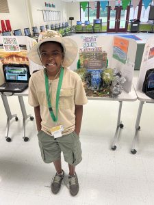 An eight year old African American boy wearing a ranger hat stands in front of a school display about the Smokies.