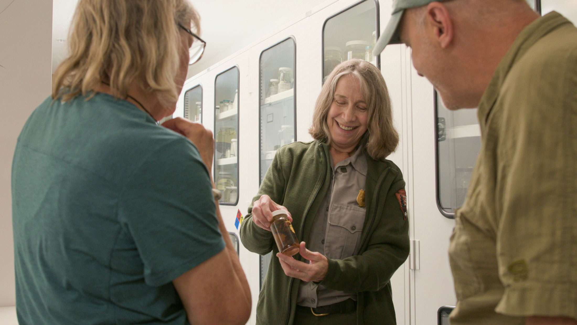 Woman in NPS jacket showing an insect specimen to a woman and man.