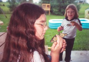 A young girl in glasses examines a monarch butterfly
