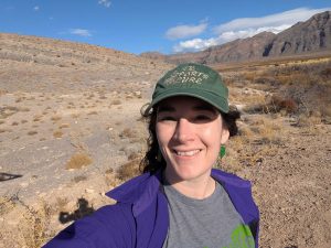 A selfie of a woman in a baseball cap with landscape in the background.