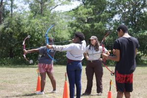 A park anger with her hands on her hips stands alongside three teenagers with bow and arrows in hand.