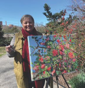A woman standing behind an easel holding a colorful landscape painting.
