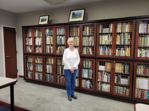A woman stands in front of a bookshelf with art above