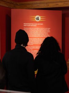 Two silhouettes in front of a red exhibit panel