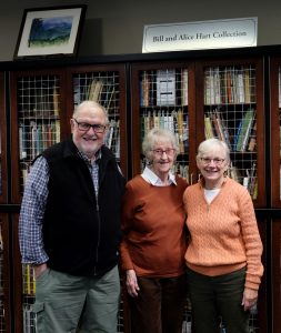 A man and two women stand together in front of a bookshelf and a sign that reads Bill and Hart Collection