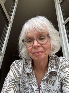 Headshot of a woman with white hair and glasses.