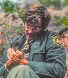 A man in a ranger jacket tenderly holding a bear cub