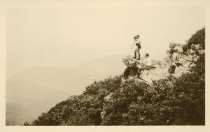 Black and white photo of two men in the distance standing on a rock with a camera