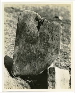 Black and white photo of a rock with a hole at the top that has been written on.
