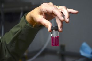 A hand holding a test tube filled with a red colored liquid
