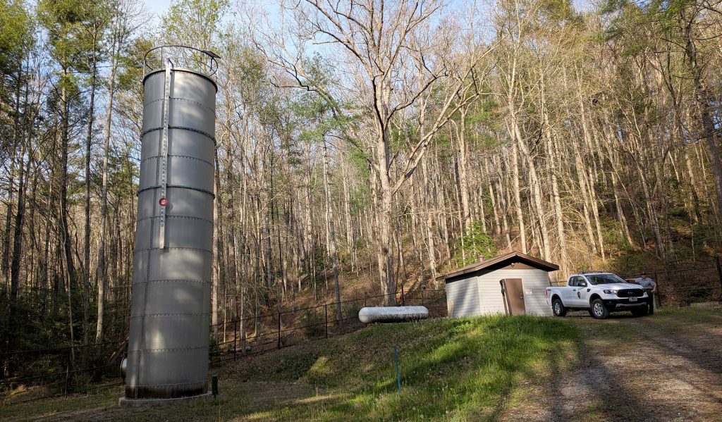 A water tower with a building and truck in the background.