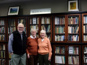 A man and two women standing in front of rows of book shelves.